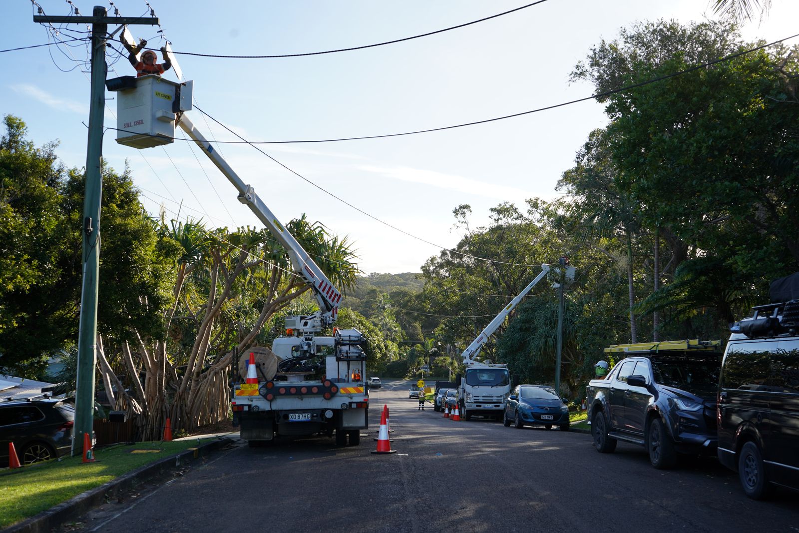 Two crews working on overhead lines along a suburban street